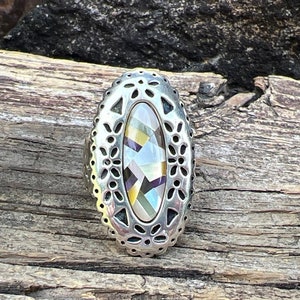 May include: A silver ring featuring an oval-shaped inlay of multicoloured abalone shell. The ring has a delicate floral design around the edge.