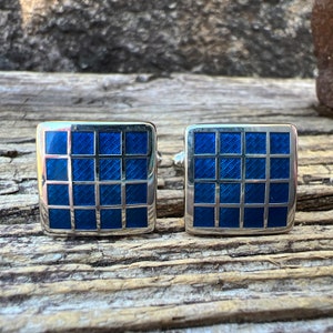 May include: A pair of silver cufflinks with a blue checkered pattern.