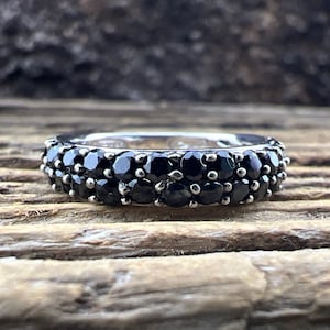 May include: A silver band ring with two rows of black gemstones. The ring is on a wooden surface.