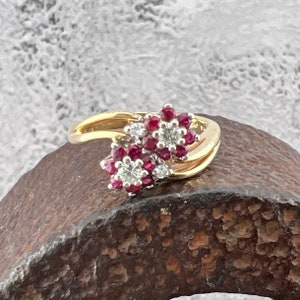 May include: A gold ring featuring two clusters of red rubies and white diamonds set in a flower design.