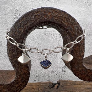 May include: A silver charm bracelet with three charms. The center charm is a diamond shape with blue sapphires. The other two charms are silver and diamond shaped.