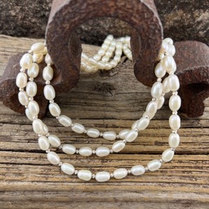 May include: A white pearl necklace with oval-shaped pearls. The necklace is draped over a rusty metal object and a wooden surface.