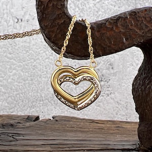 May include: A gold necklace with a double heart pendant. The hearts are intertwined and have a diamond-like pattern.