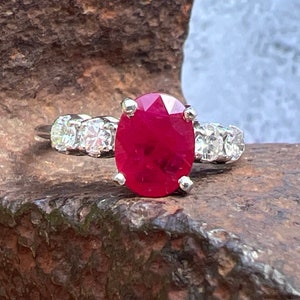 May include: A ring with a large oval ruby gemstone surrounded by a band of smaller diamonds.