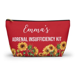 Pode incluir: Uma bolsa vermelha com zíper com o texto "Emma's ADRENAL INSUFFICIENCY KIT" em branco. A bolsa é decorada com uma fileira de girassóis amarelos na parte inferior. O zíper é dourado.
