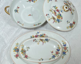 May include: A set of three white porcelain serving dishes with a floral and bird design. The dishes are decorated with red, yellow, blue, and green flowers and birds. The dishes are oval and round in shape.