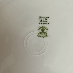 Puede incluir: Un plato de cer&aacute;mica blanco con un logotipo verde que dice "Limoges France Unique" y "U.C. France" en una fuente m&aacute;s peque&ntilde;a.