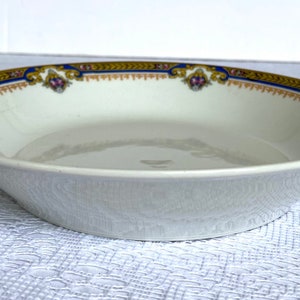Puede incluir: Un taz&oacute;n de cer&aacute;mica blanca con un borde azul y dorado y un dise&ntilde;o floral. El taz&oacute;n est&aacute; vac&iacute;o y se encuentra sobre un mantel blanco.