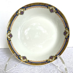 Puede incluir: Un taz&oacute;n de sopa de cer&aacute;mica blanca con un borde floral azul y dorado. El taz&oacute;n tiene un delicado patr&oacute;n floral con acentos rosados, azules y dorados.