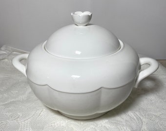 May include: White porcelain soup tureen with a lid and two handles. The lid has a small flower-shaped knob.
