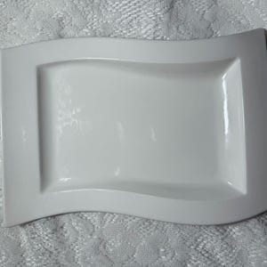 May include: A white ceramic serving platter with a wavy edge. The platter is rectangular with a slightly raised rim.