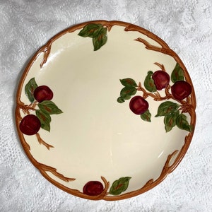 May include: A white ceramic dinner plate with a brown rim and a design of red plums and green leaves on a brown branch.