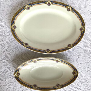 May include: Two oval serving platters. The larger platter is approximately 16 inches long, and the smaller one is about 9 inches long. Both have a cream-colored surface with a decorative border of gold, blue, and purple accents.