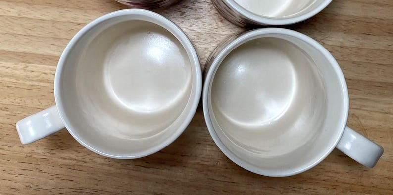 May include: Four white ceramic mugs with a handle on the side. The mugs are empty and have a smooth, glossy finish.