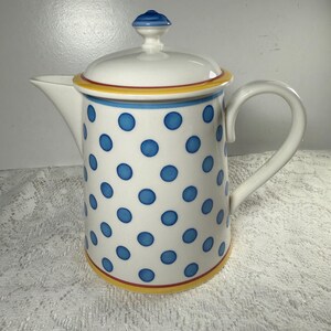 May include: White ceramic coffee pot with a lid and handle. The pot is decorated with blue polka dots and has yellow and red trim. The lid has a blue finial. The pot is designed for serving coffee or tea.