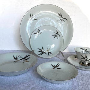 Puede incluir: Un juego de vajilla de cerámica blanca con un diseño de bambú plateado. El juego incluye un plato de cena grande, un plato para ensalada, un tazón de sopa, un plato para pan y mantequilla, una taza de té y un platillo.