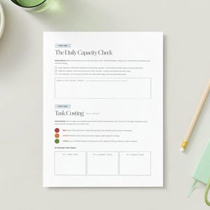 Pode incluir: Um papel branco intitulado "The Daily Capacity Check" com instru&ccedil;&otilde;es e se&ccedil;&otilde;es de c&aacute;lculo de tarefas. Um l&aacute;pis, um pequeno caderno verde e um molho de chaves est&atilde;o &agrave; direita. Uma tigela de uvas verdes e um copo de &aacute;gua est&atilde;o &agrave; esquerda.