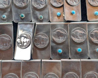 May include: A collection of silver-toned metal money clips. Some clips feature a profile of a Native American man, while others display a buffalo. Several clips have a small turquoise stone. The clips are arranged in rows.