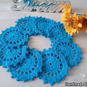 Könnte beinhalten: Ein Set aus zehn gehäkelten Untersetzern in Türkisblau, die in einem Kreis angeordnet sind. Die Untersetzer sind handgefertigt und haben ein zartes Blumenmuster.