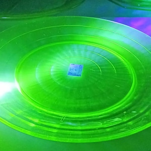 May include: A bright green glass plate with a concentric circle design. The plate is illuminated by a bright light source.