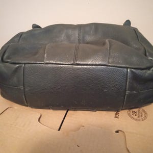 May include: A dark gray leather handbag with a textured surface. The bag has a rectangular base and a rounded top with two small handles. The stitching is visible along the seams.