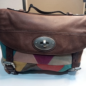 May include: A brown leather Fossil handbag with a patchwork design in shades of pink, red, green, and blue. The bag has a silver buckle and a silver Fossil logo.