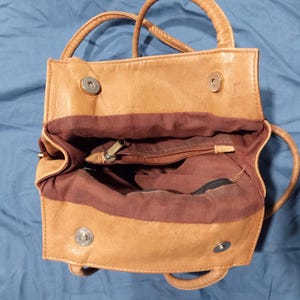 May include: A tan leather handbag with a brown fabric lining. The bag has two top handles and a zipper closure.
