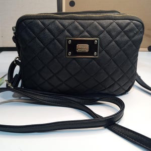 May include: Black quilted crossbody bag with a gold zipper and a gold metal plate with the text "Steve Madden" on it.