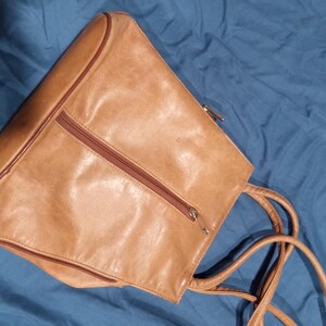 May include: A tan leather tote bag with two zippered compartments and a long strap.