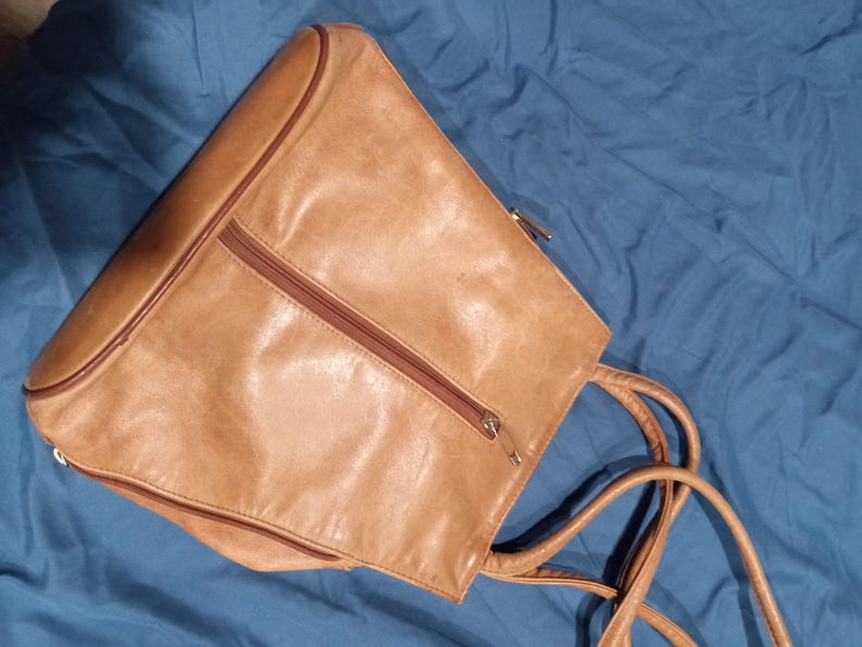 May include: A tan leather tote bag with two zippered compartments and a long strap.