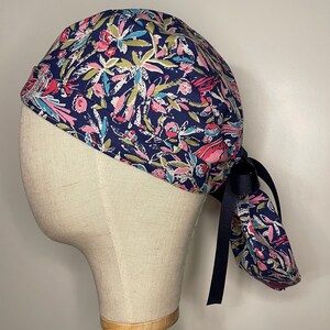 May include: A blue surgical scrub hat with a colorful floral pattern. The hat has a tie on the back.