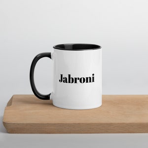 May include: White ceramic mug with a black rim and handle. The mug has the word "Jabroni" printed in black bold letters.