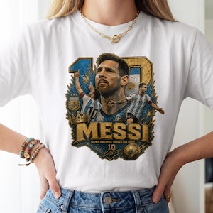 May include: A white t-shirt featuring a graphic print of Lionel Messi. The design includes a large portrait of the player, two action shots, the number 10, a gold crown, a soccer ball, and the text MESSI, TALENTO SEM LIMITES, LENDARIO PARA SEMPRE.