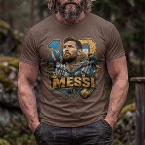 May include: A brown short-sleeved t-shirt featuring a graphic print of Lionel Messi. The design includes the number 10, the name MESSI in gold lettering, and images of the player in an Argentina jersey against a blue and gold background.