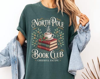 Könnte beinhalten: Dunkelgrünes T-Shirt mit dem Schriftzug "North Pole Book Club" in dekorativer Schrift. Die Grafik zeigt eine Kaffeetasse, Bücher und Blätter. Der Satz "Cheerful Escape" steht unter den Worten "Book Club".