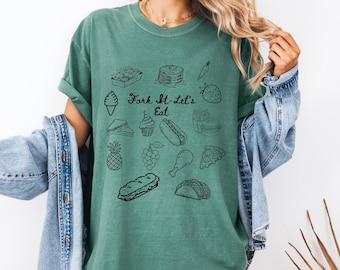Peut inclure: T-shirt vert d'eau avec l'inscription "Fork It-Let's Eat" et des illustrations noires d'aliments. On y voit une glace, des crêpes, une fraise et d'autres images d'aliments. Le t-shirt est de couleur unie.