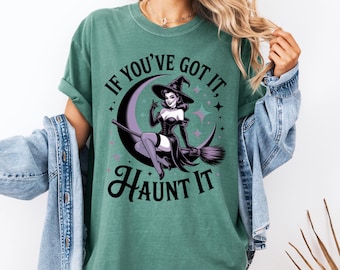 May include: Green t-shirt with the text "IF YOU'VE GOT IT, HAUNT IT" and a graphic of a witch on a broomstick. The witch is wearing a black dress, hat, and gloves, and is seated on a crescent moon. The design includes stars.