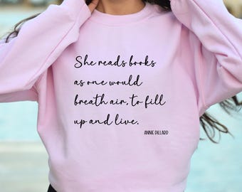 May include: A pink sweatshirt with the quote "She reads books as one would breath air, to fill up and live." by Annie Dillard.