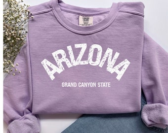 May include: A lavender sweatshirt with the text "Arizona Grand Canyon State" in white distressed lettering.