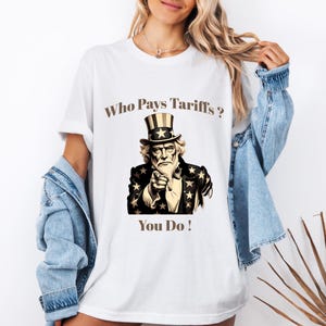 May include: White t-shirt featuring a graphic of Uncle Sam pointing, with the text "Who Pays Tariffs? You Do!" in brown. The Uncle Sam illustration is in black, brown, and white, with a star-studded jacket and top hat.
