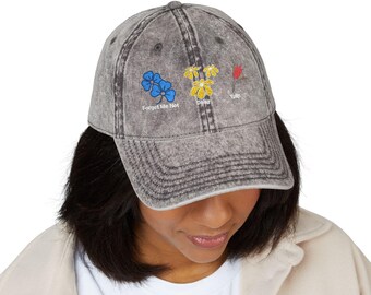 May include: A gray baseball cap with embroidered floral designs. The cap features blue Forget Me Not flowers, yellow Daisies, and a red Tulip. The text "Forget Me Not", "Daisy", and "Tulip" are embroidered below each flower.