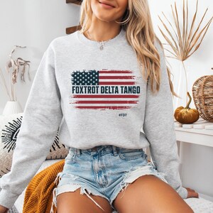 May include: A grey sweatshirt with a distressed American flag graphic and the text "FOXTROT DELTA TANGO" and "#FDT".