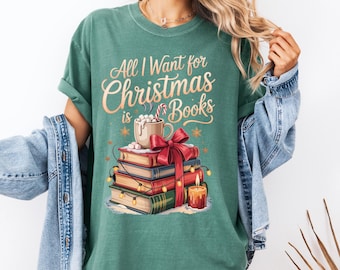 May include: Green t-shirt with the text "All I Want for Christmas is Books." The graphic features a stack of books tied with a red bow, a mug of hot chocolate, and a lit candle. Festive holiday apparel.