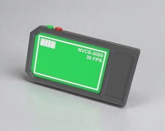 Könnte beinhalten: Ein rechteckiges, dunkelgraues elektronisches Gerät mit einem hellgrünen Bildschirm. Das Display zeigt ein weißes Batteriesymbol, den Text NVCS-3000 und 30 FPS. Zwei kleine runde Tasten, eine grüne und eine rote, befinden sich an der Oberkante.