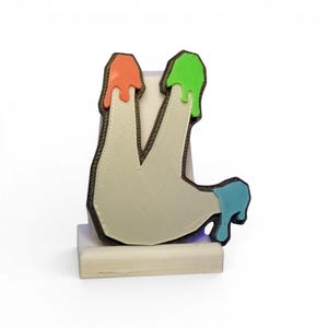May include: A white, stylized letter "L" with a black outline, standing on a small, rectangular base. The top of the letter has orange and green drips, and the bottom has blue drips. The design is 3D printed.