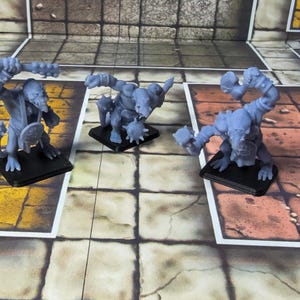 May include: Three grey, unpainted miniature figures of rat-like creatures standing on black square bases. Each figure is in a dynamic combat pose, holding a spiked mace or club in one hand and a small round shield in the other, with detailed tails.