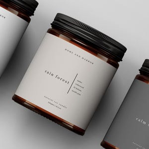 以下が含まれることがあります： 黒い蓋と白いラベルが付いた3つのガラス瓶。ラベルには「campfire」、「rain forest」、「calm seas」と書かれています。瓶には「HOME AND HARBOR」のラベルが貼られており、天然大豆ワックスキャンドルが充填されています。画像には「MADE IN Canva」のロゴも含まれています。