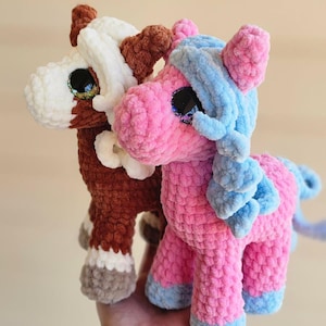 May include: Two plush toy horses. One is brown and white, the other is pink and blue. Both have large, glittery eyes. The toys are made of a soft, textured material, and are likely handmade.
