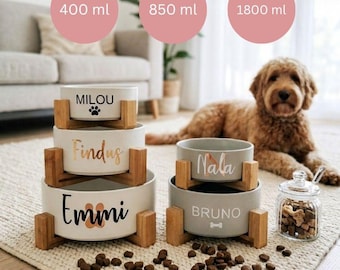 Puede incluir: Un conjunto de cuencos personalizados para mascotas en blanco y gris, con soportes de madera. Los cuencos están etiquetados con nombres de mascotas en varias fuentes. La imagen muestra cuencos con capacidades de 400 ml, 850 ml y 1800 ml. Un perro y un tarro de golosinas también están en la imagen.