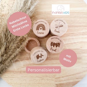 Pode incluir: Quatro caixas de madeira com tampas, cada uma decorada com um design diferente e personalizada com um nome. Os designs incluem um arco-íris, uma tesoura, um dente e um elefante. As caixas estão etiquetadas "Nabelschnur von Emma", "Erste Locke von Noah", "Milchzähne von Pant", e "Erste Locke von Sophia". As caixas estão sobre uma superfície de madeira com um fundo rosa.